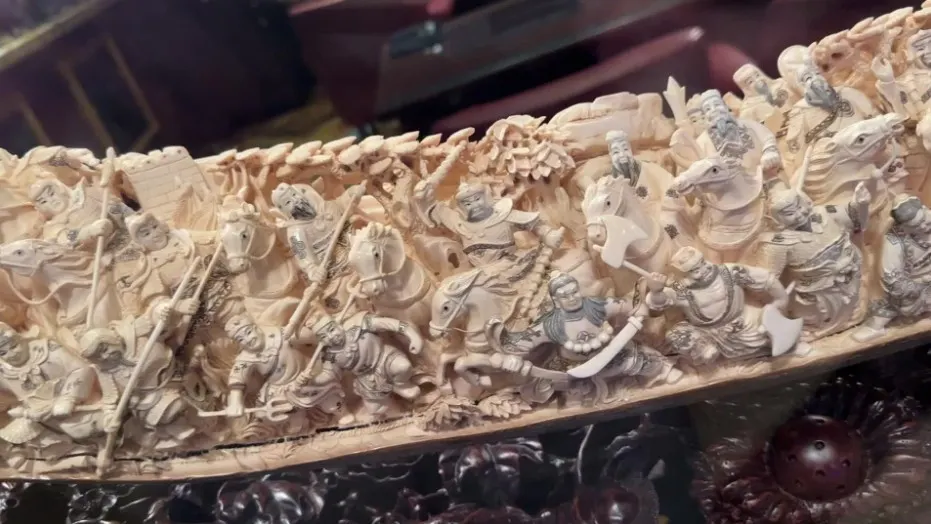 An up close pic of the carved tusk that shows the detailed people, animals, and structures. 