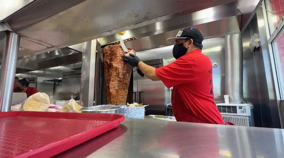 An employee cuts pork off of a spinner. 
