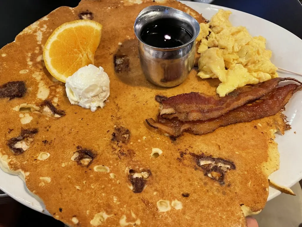 Snickers twisted flapjack, 2 slices of bacon, and scrambled eggs on a plate