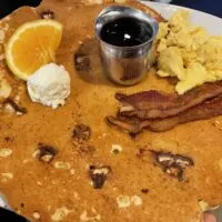 Snickers twisted flapjack, 2 slices of bacon, and scrambled eggs on a plate