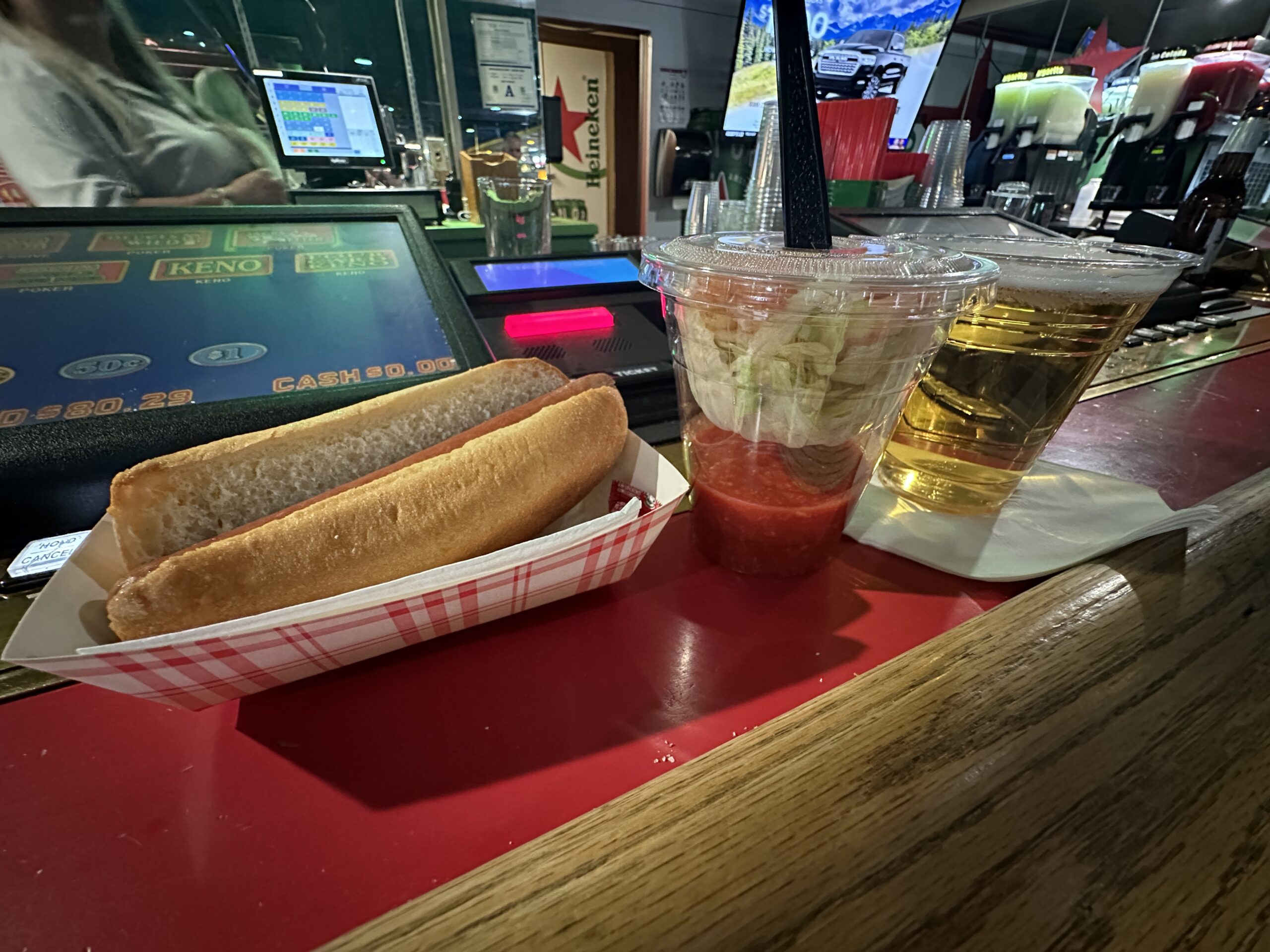 A hot dog, shrimp cocktail, and draft beer lined up on the bar counter.