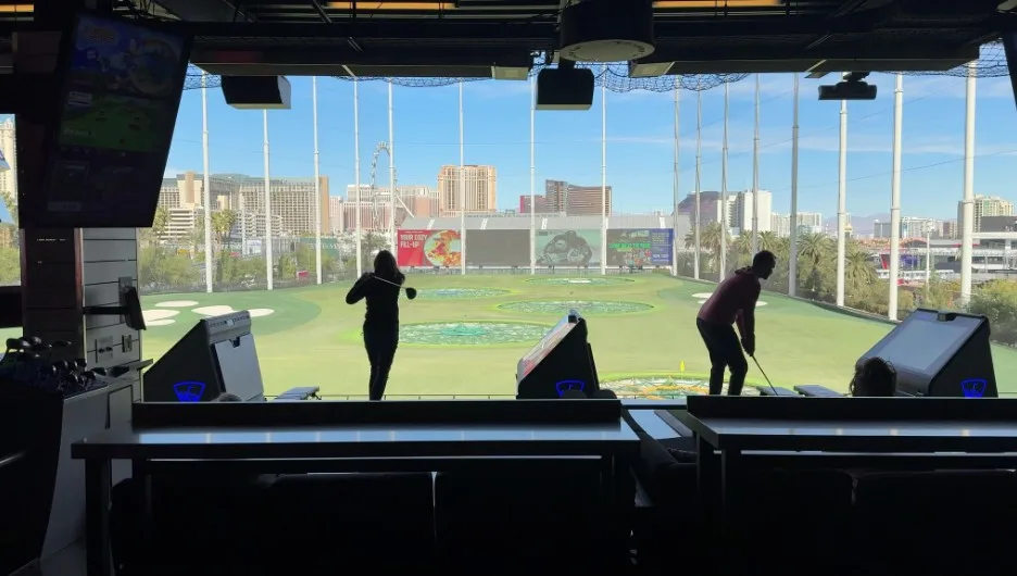 2 golfers, silhouetted against the backdrop of the range. 