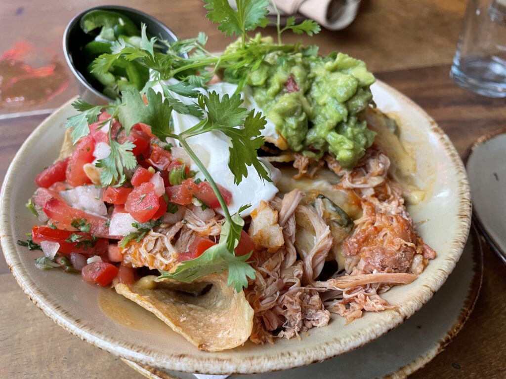 A bowl of nachos topped with guac, pico, chicken, cheese, and sour cream.