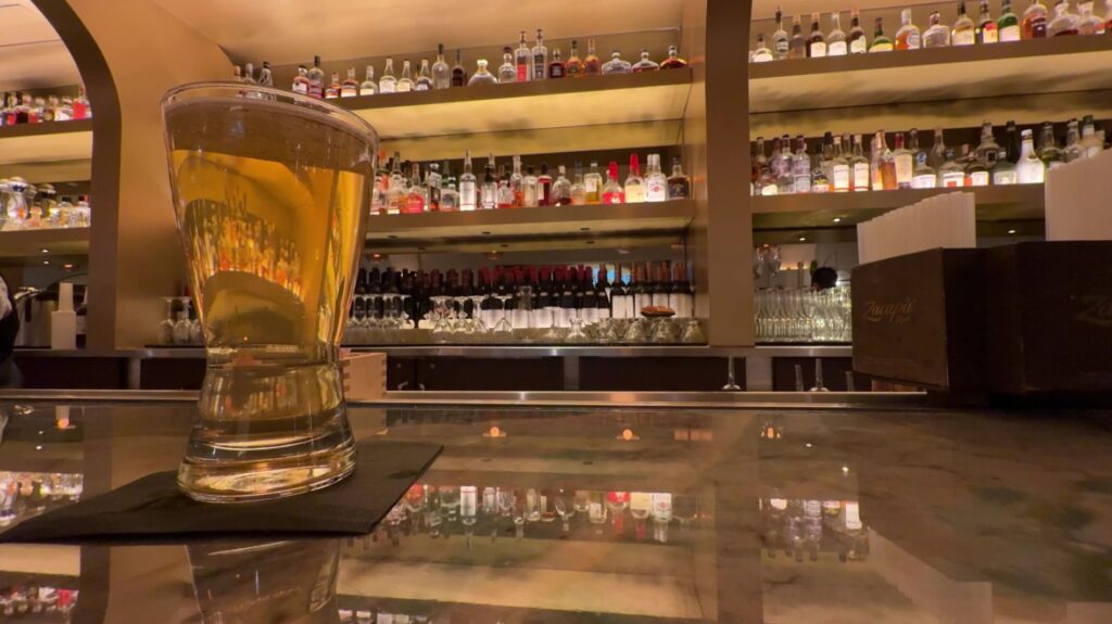 A draft beer on the bar with illuminated bottles on a shelf in the background.