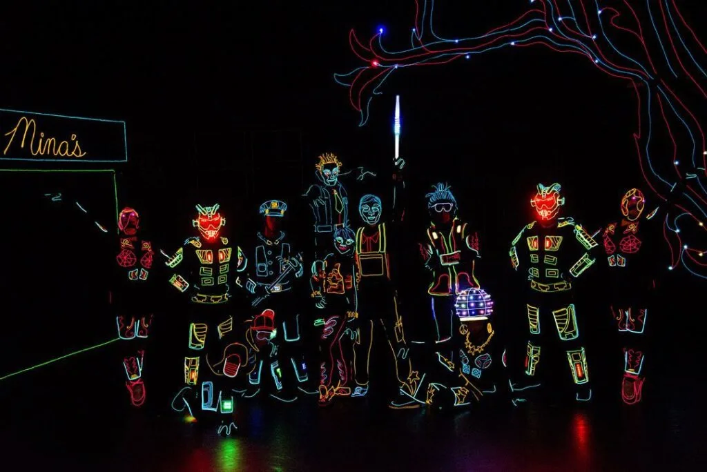 Dancers stand on a dark stage wearing costumes with LED lighting features