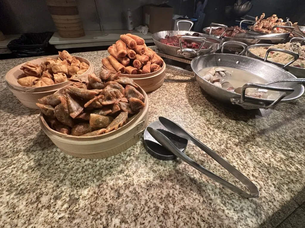 A large selection of Asian dishes that include potstickers, spring rolls, garlic clams, and carved duck roast.