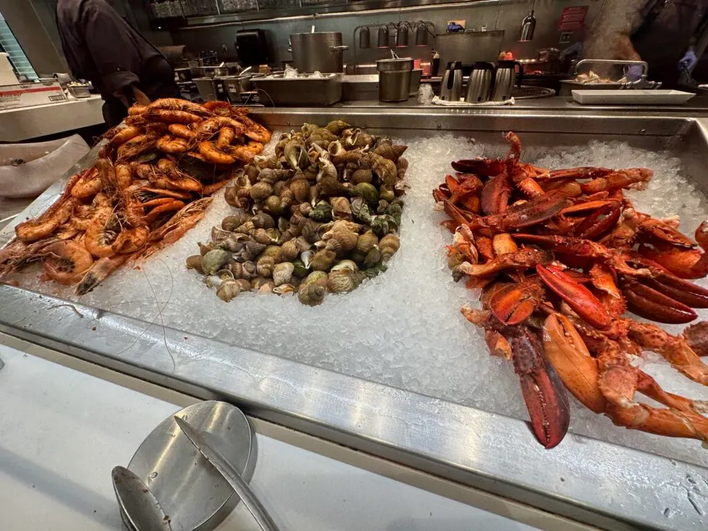 Cajun poached prawns, whelks, and Lobster Claws piled up separately on a bed of ice.