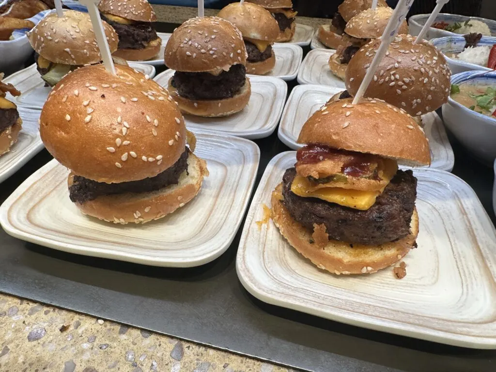 Individual plates lined up, each with a small hamburger on it.