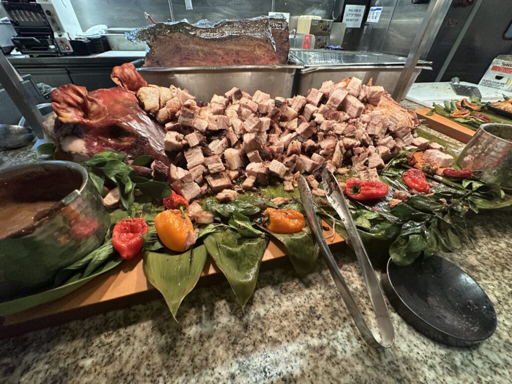 An entire roasted pig, which has been cubed after cooking is on display with serving tongs.