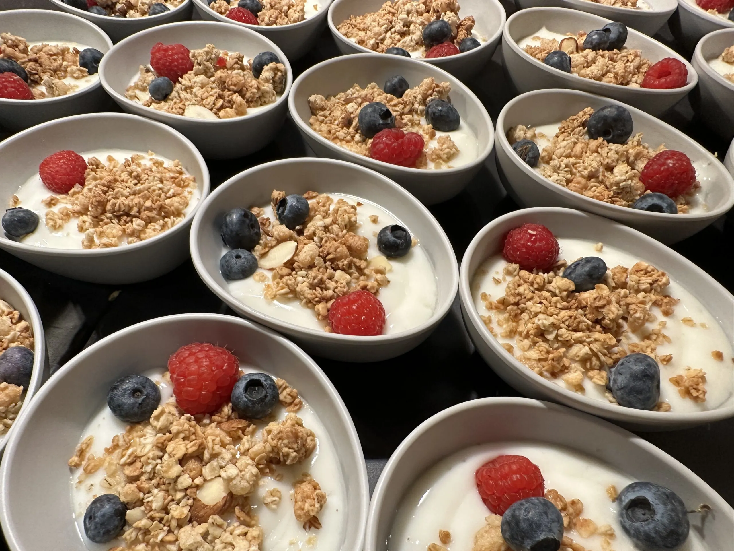 Individual yogurt bowls topped with granola, blueberries, and raspberries.