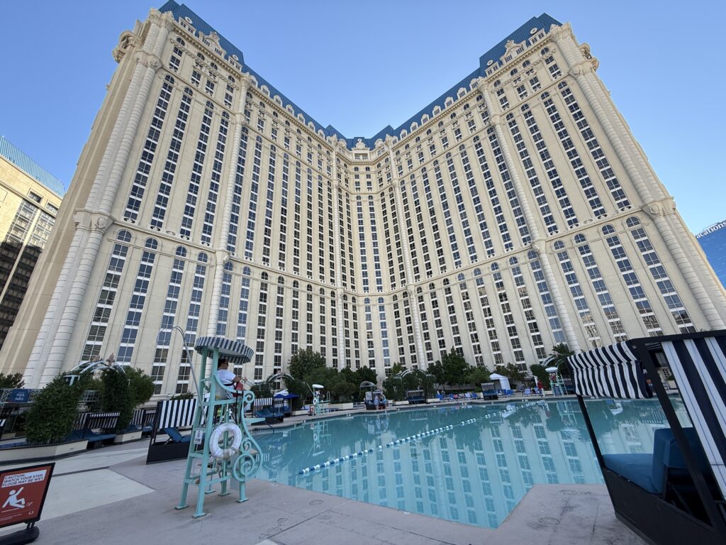 The pool at paris in the foreground, with the main hotel tower extending into the blue sky behind it. 