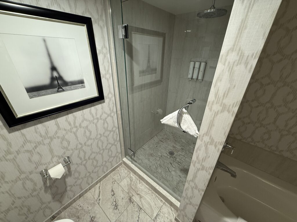 A portrait of the Eiffel Tower hangs next to a glass enclosed shower. 