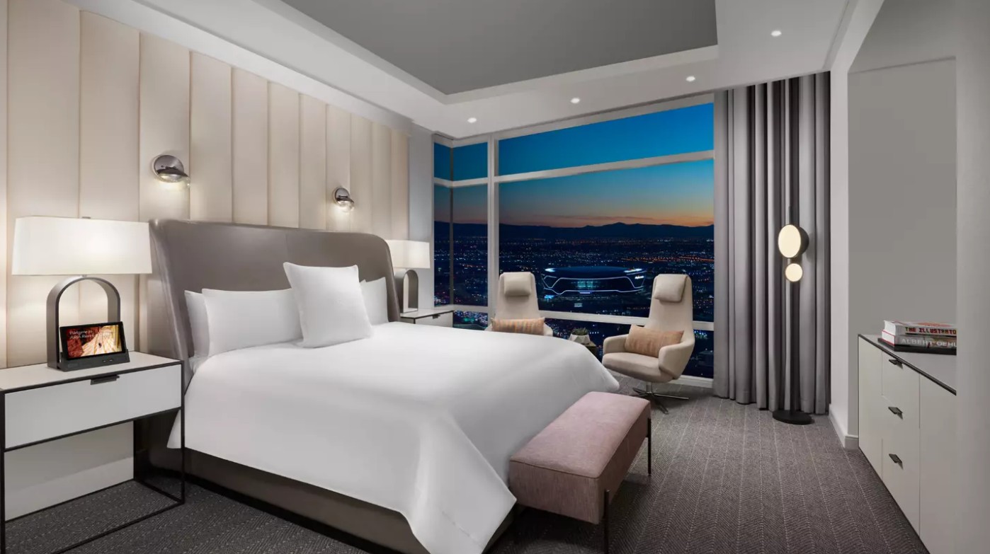 A bed pushed up against a white padded headboard, topped and flanked by decorative lighting.