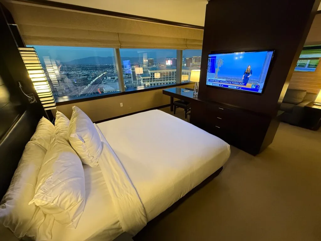 A bed pointed at a TV hanging on a partial partitian that separates the bedroom from the living area. 