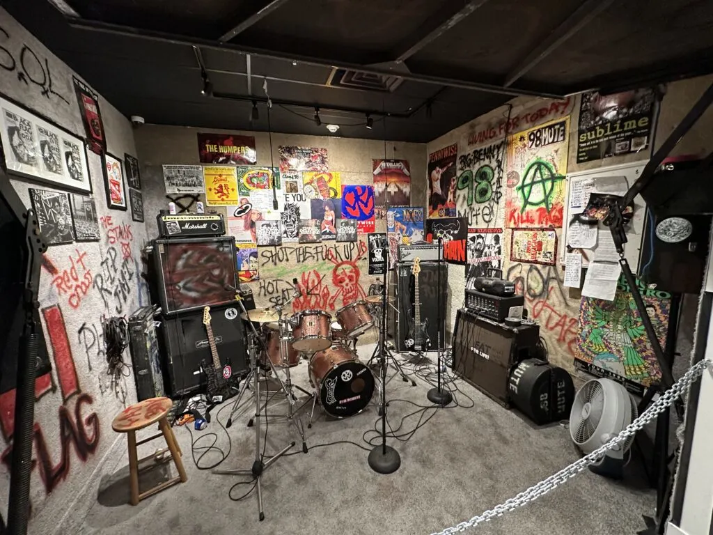 A garage band setup with drums, guitars, speakers, and posters on the walls. 