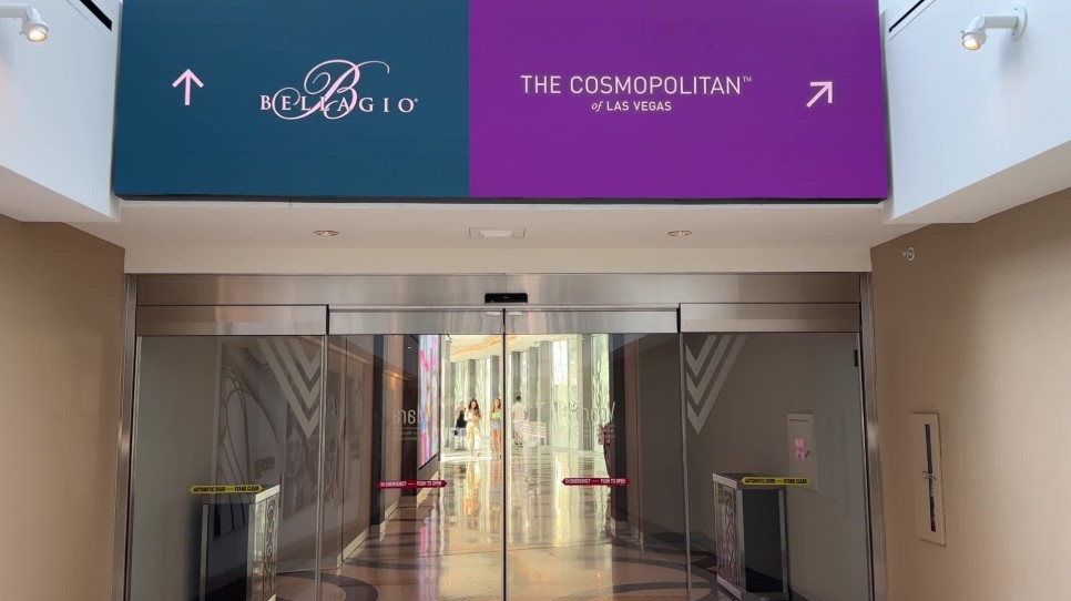 A walkway, with a sign hanging above it with arrows directing you to either Bellagio or Cosmopolitan. 