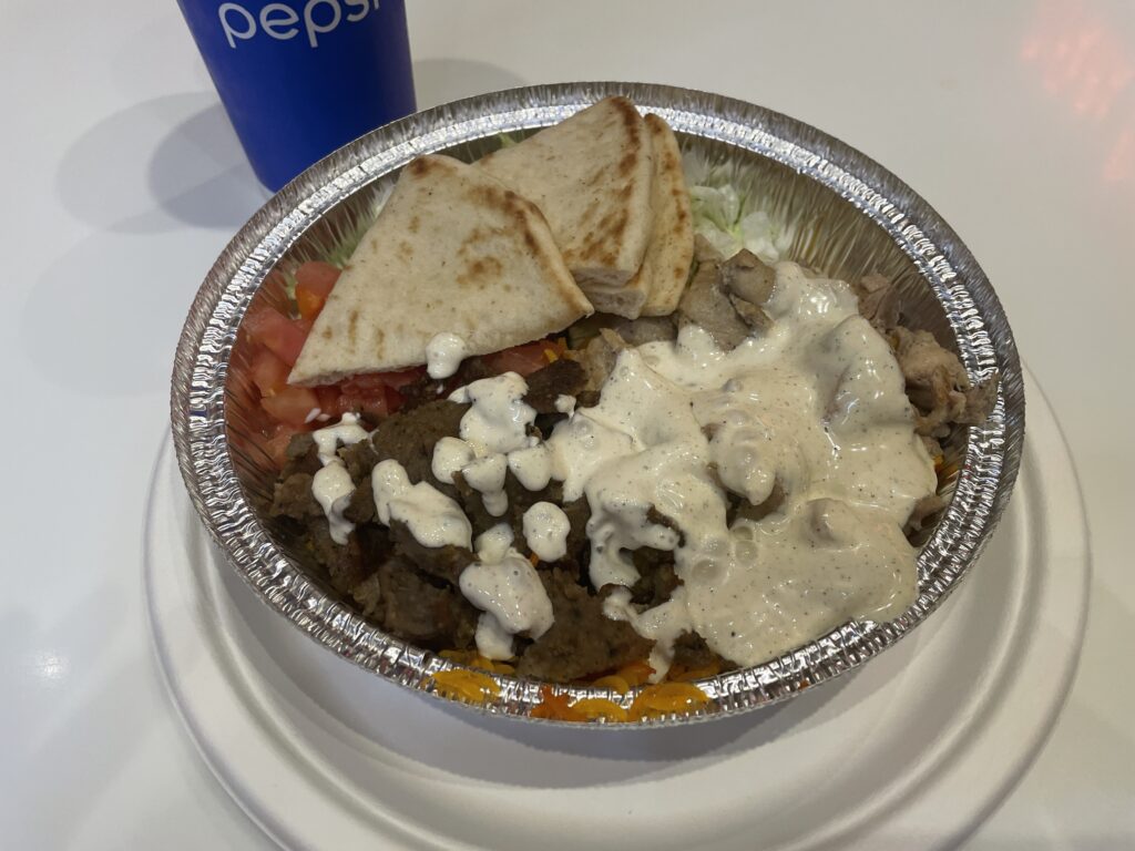 A gyro bowl from the halal guys that has meat, rice, hot sauce, tomatoes, and pita triangles.