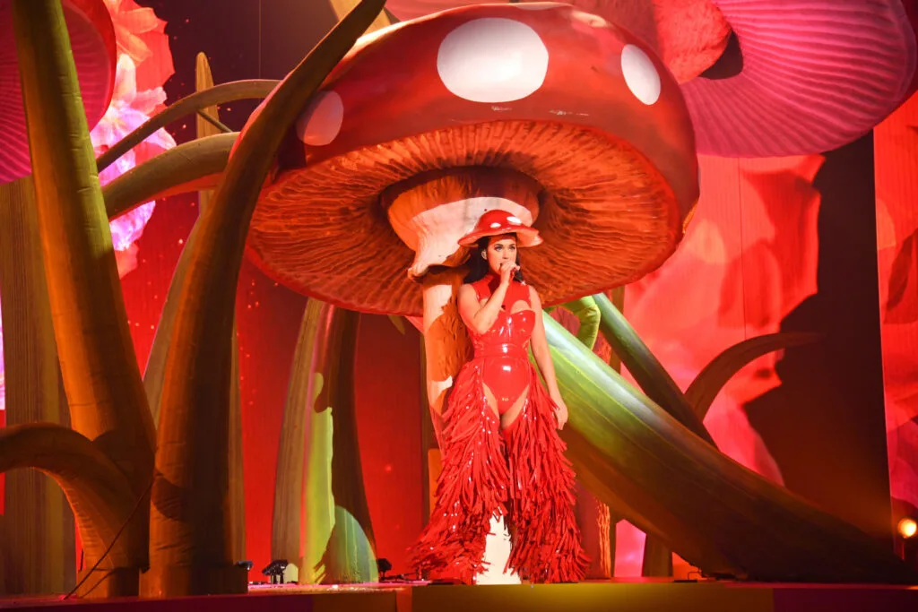 Katy Perry performs in front of a picture of a giant red and white mushroom.