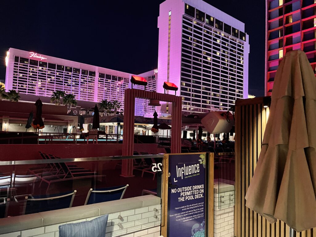 Poolside cabana at night with Flamingo illuminated pink in the background