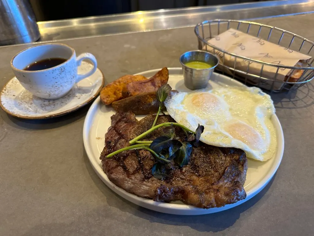 A large ribeye steak sharing a plate with two over easy eggs and potatoes. 