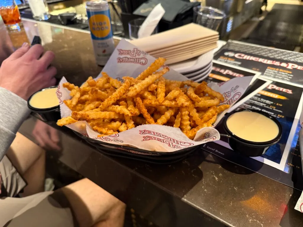 A basket of seasoned crabfries, with two little tubs of white liquid cheese. 