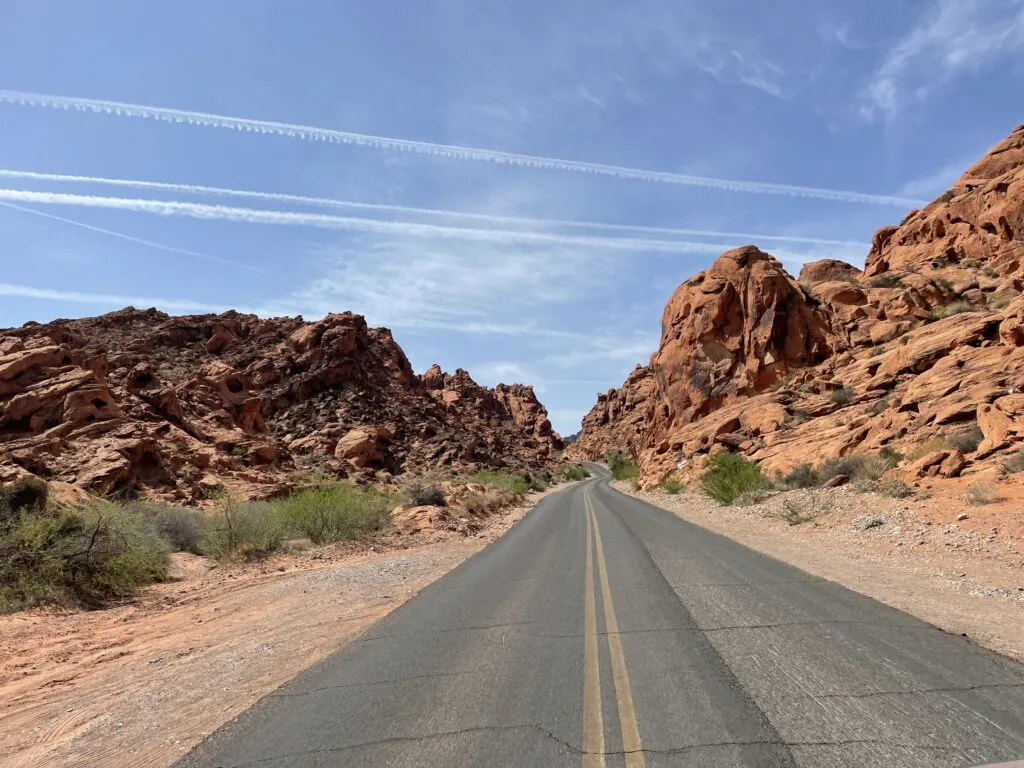 A road surrounded by red rocks on either side with a blue sky above. 