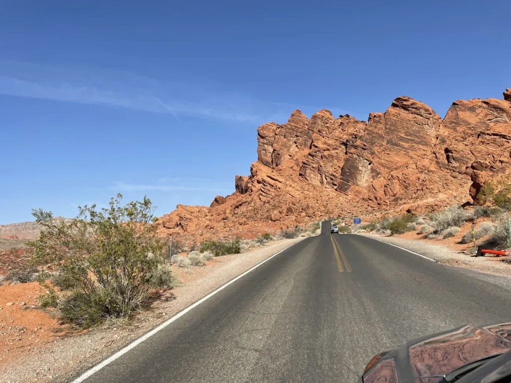 View of the road in the foreground and a bright red rock formation behind