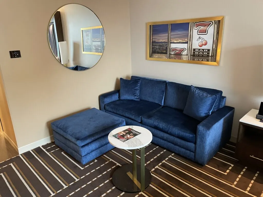 A couch, small round table. Artwork depicting slot machine reels is hanging above the couch