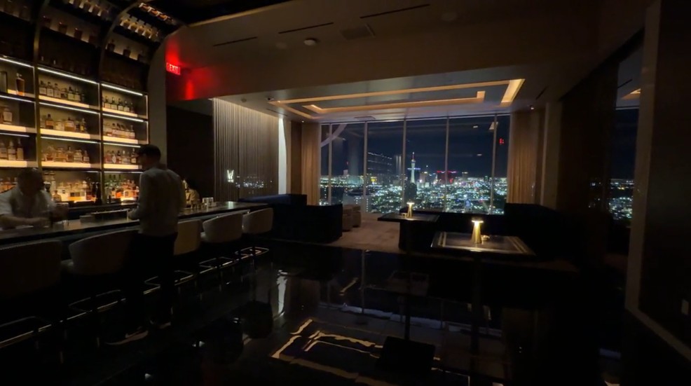 A dark, wooden lounge with a window that has a view of the Strip at night. 