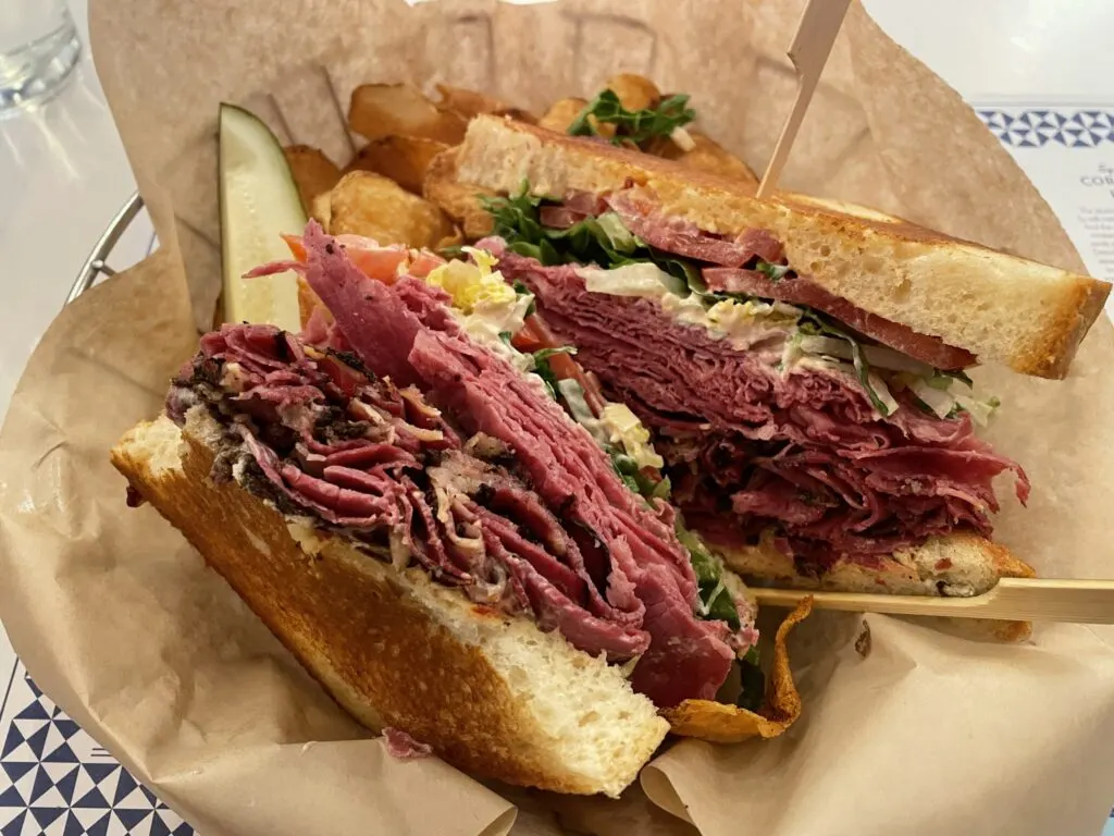 Corned Beef and pastrami sandwich in a basket with a pickle and chips