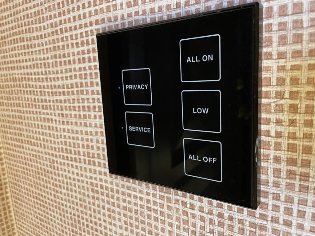 Black electronic control panel with options to turn all lights on, off, or on low. Also on the panel is the option to request privacy or service. 