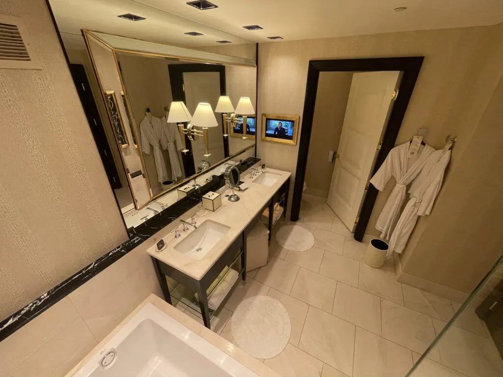 Dual vanity sink with a separate water closet. Beside the vanity is a small TV turned on