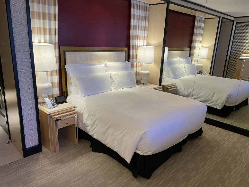 King bed flanked by lamps. Behind the bed is a maroon wall with faux drapes in the open position. 