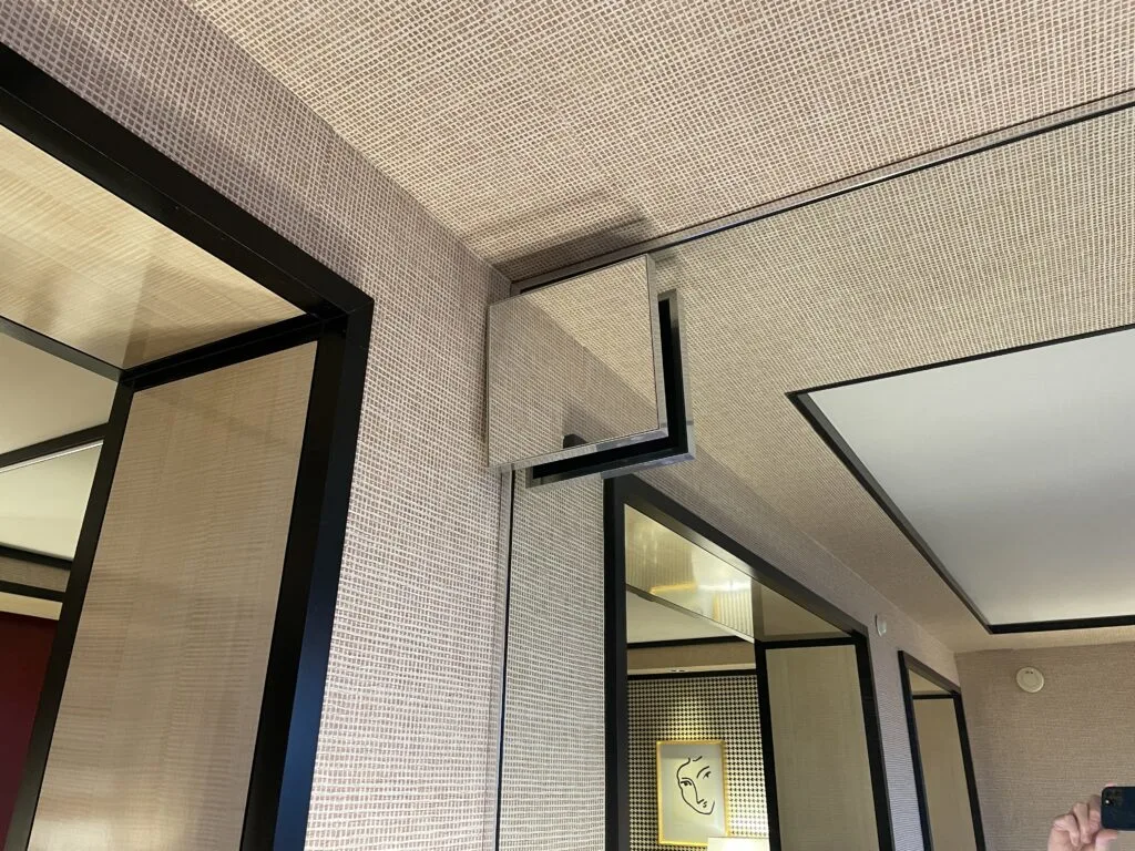 A small mirror conceals a vent hiding behind it to make it blend into the larger mirrored wall