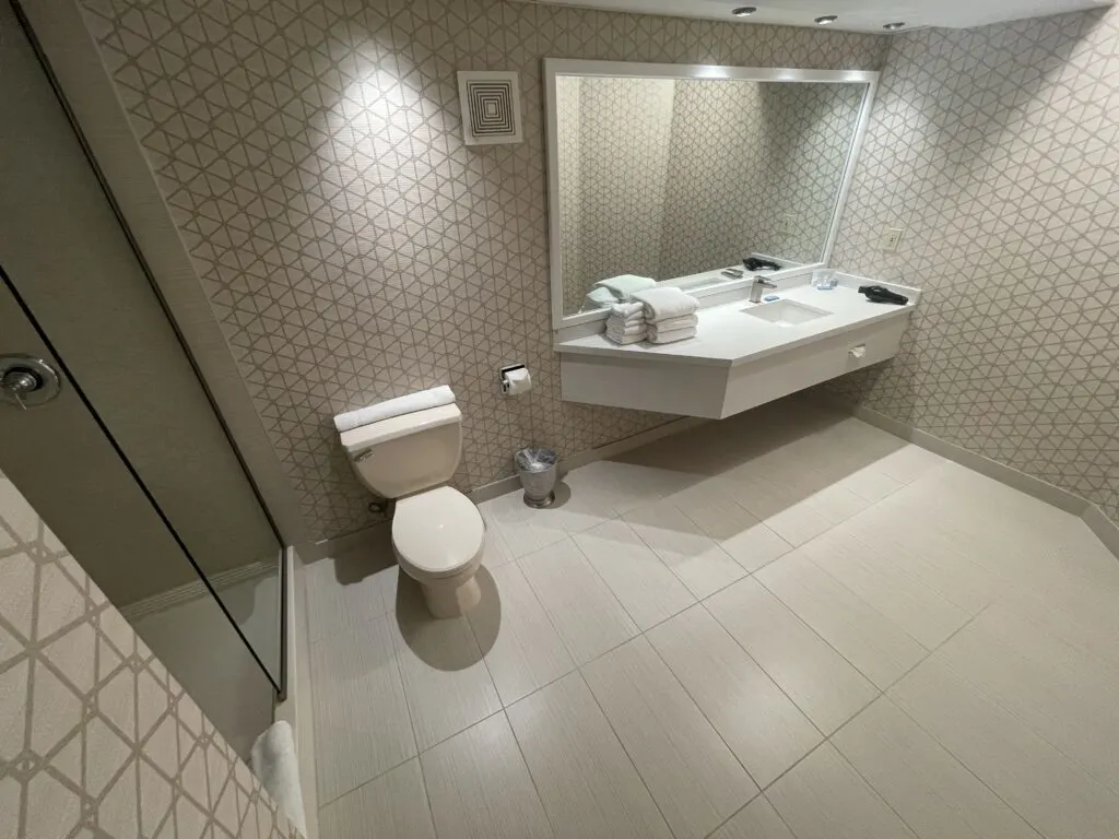 The bathroom featuring a shower to the left, a toilet, and a single sink vanity to the right