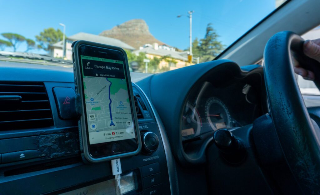 A smartphone is mounted on a car's dashboard providing directions via a maps application