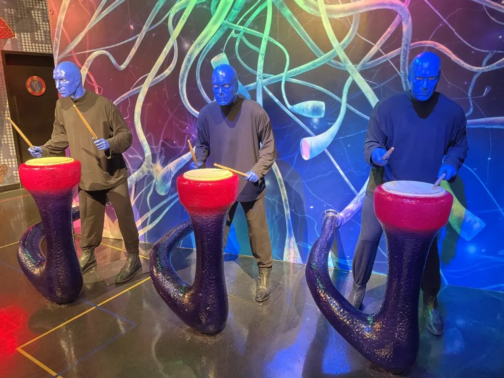 Wax figures of the Blue Man Group play red drums.