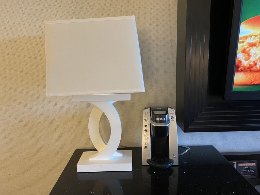 A Keurig coffee machine sits on a counter next to a white desk lamp. 