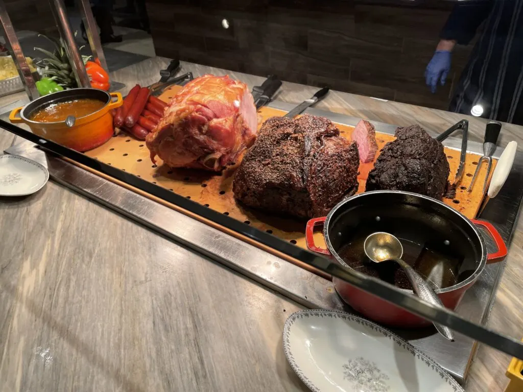 Sausage, a large ham, and top round steak on a cutting board. 