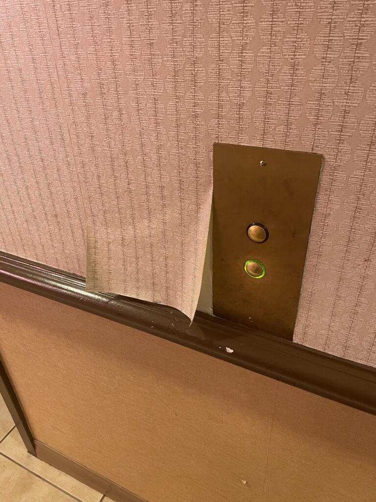 Wallpaper peeling from the wall next to an elevator button