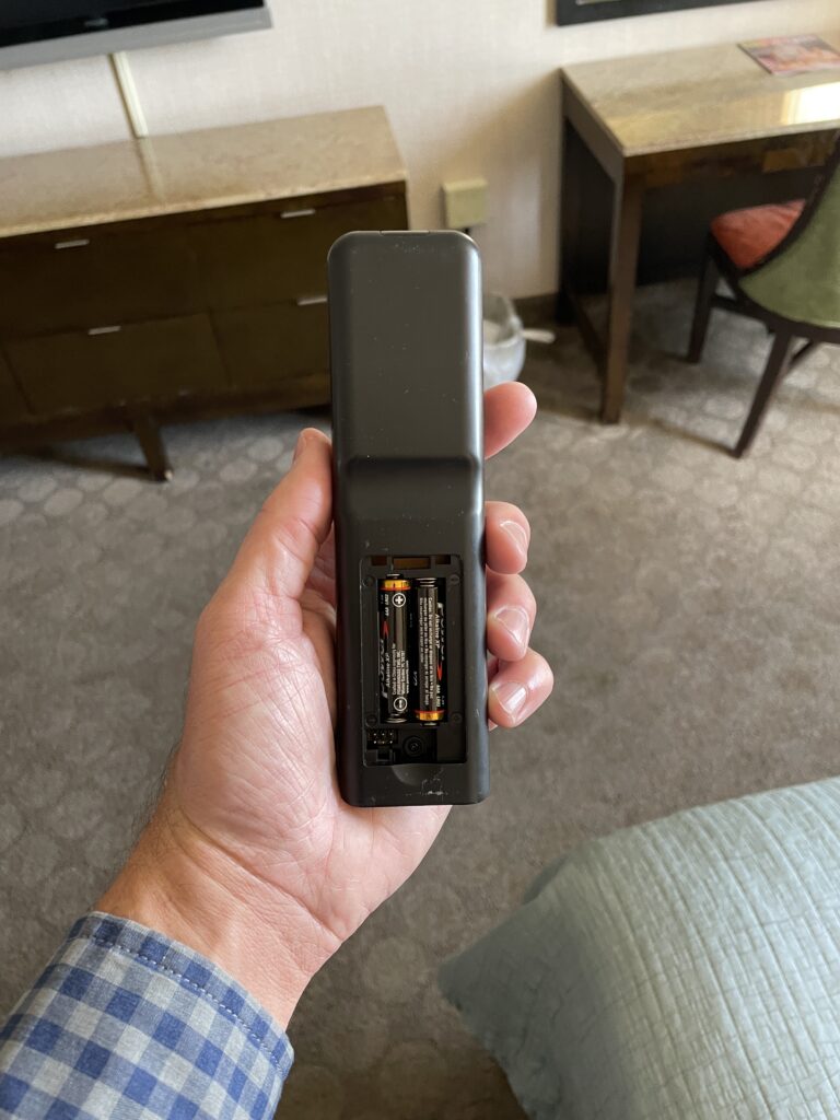 The back of a TV remote with the battery cover missing being held in my left hand.