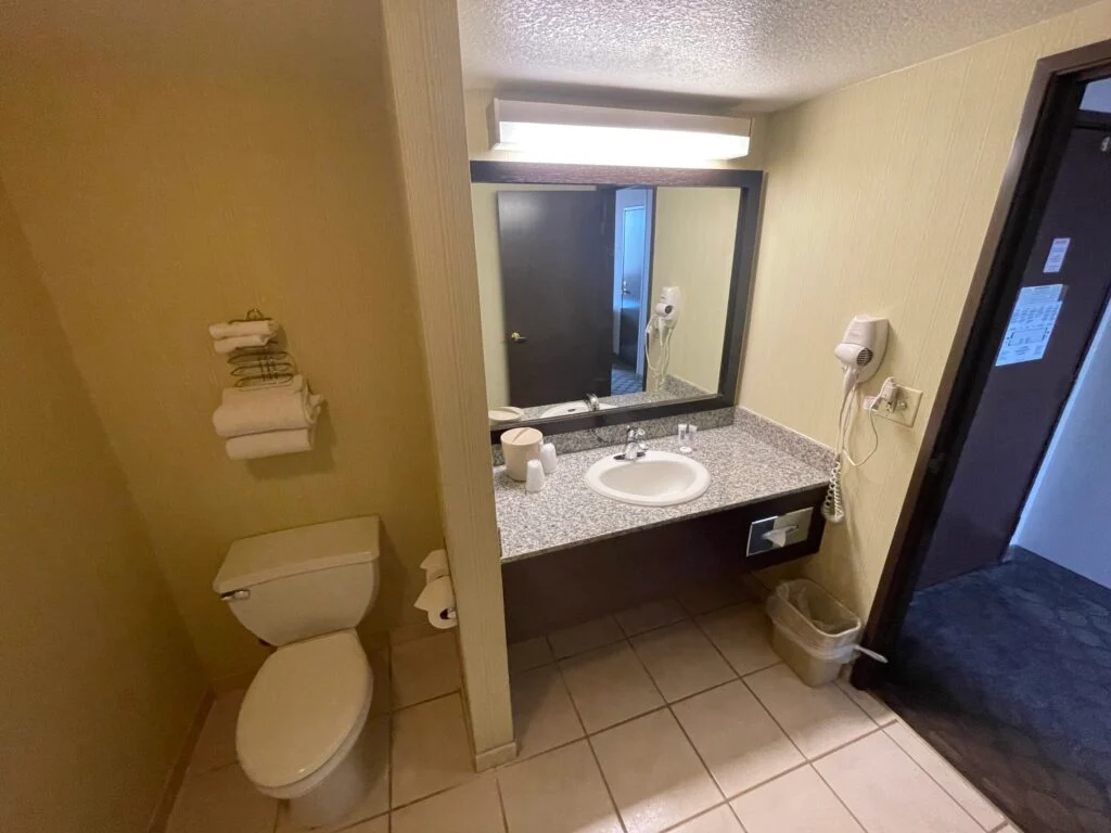 Toilet with several towels folded on a rack above it and single sink vanity to the right.