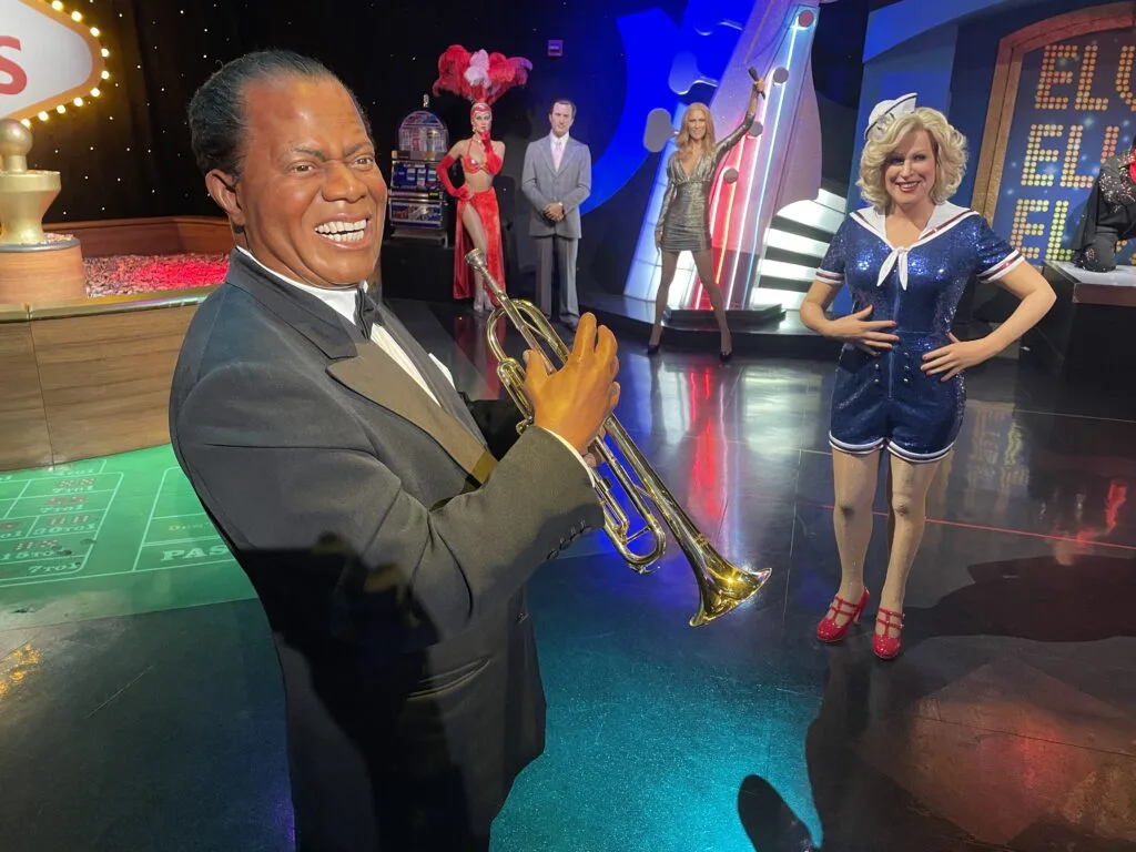 A wax figure of Louis Armstrong smiles and holds a trumpet in both hands.