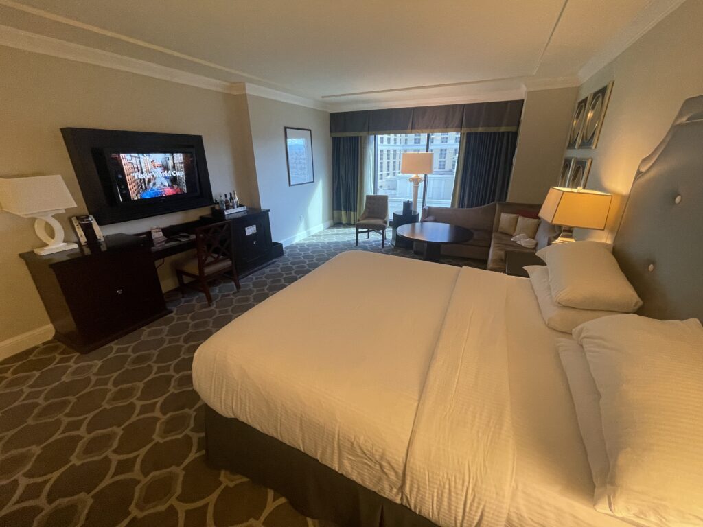 Anohter angle of the hotel room showing the king bed in the foregorund facing a wall mounted TV. An open window is in the background.