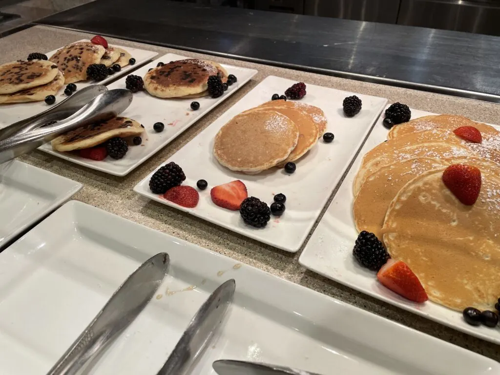 Plates full of pancakes with fruit on the edges of the plate