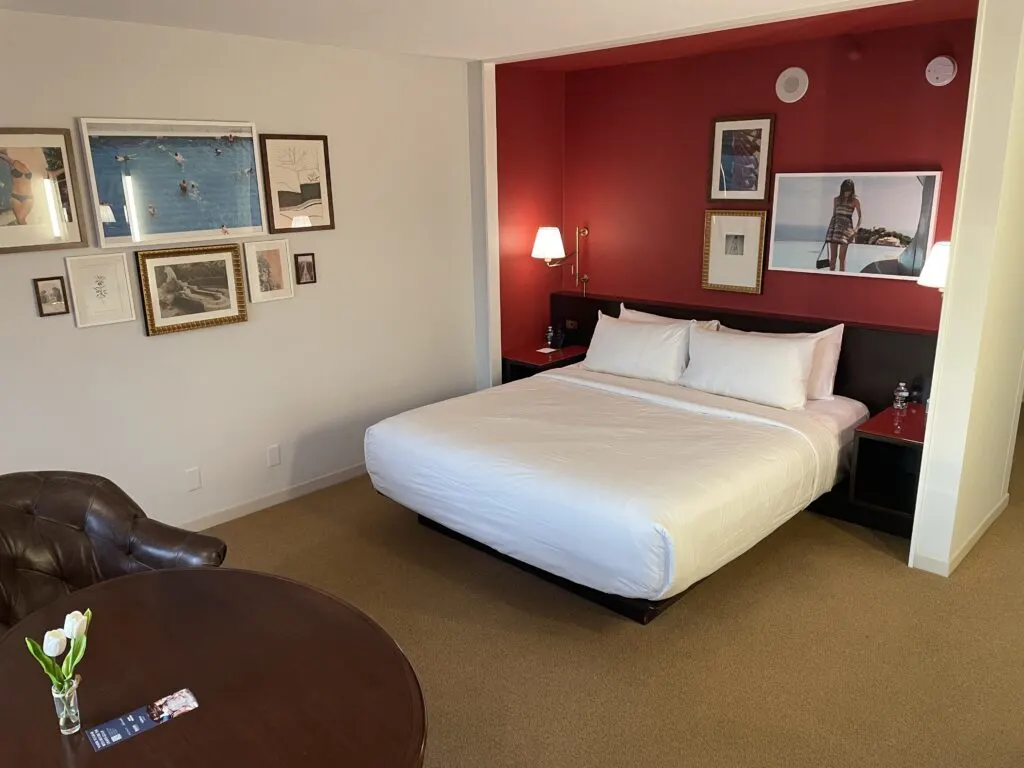 King bed with white linins and 4 pillows with a red accent wall behind it.