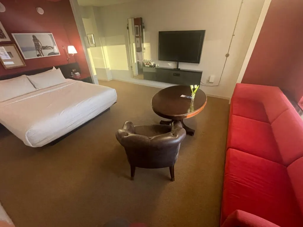 Hotel room with a king bed, small table, leather chair and red couch.