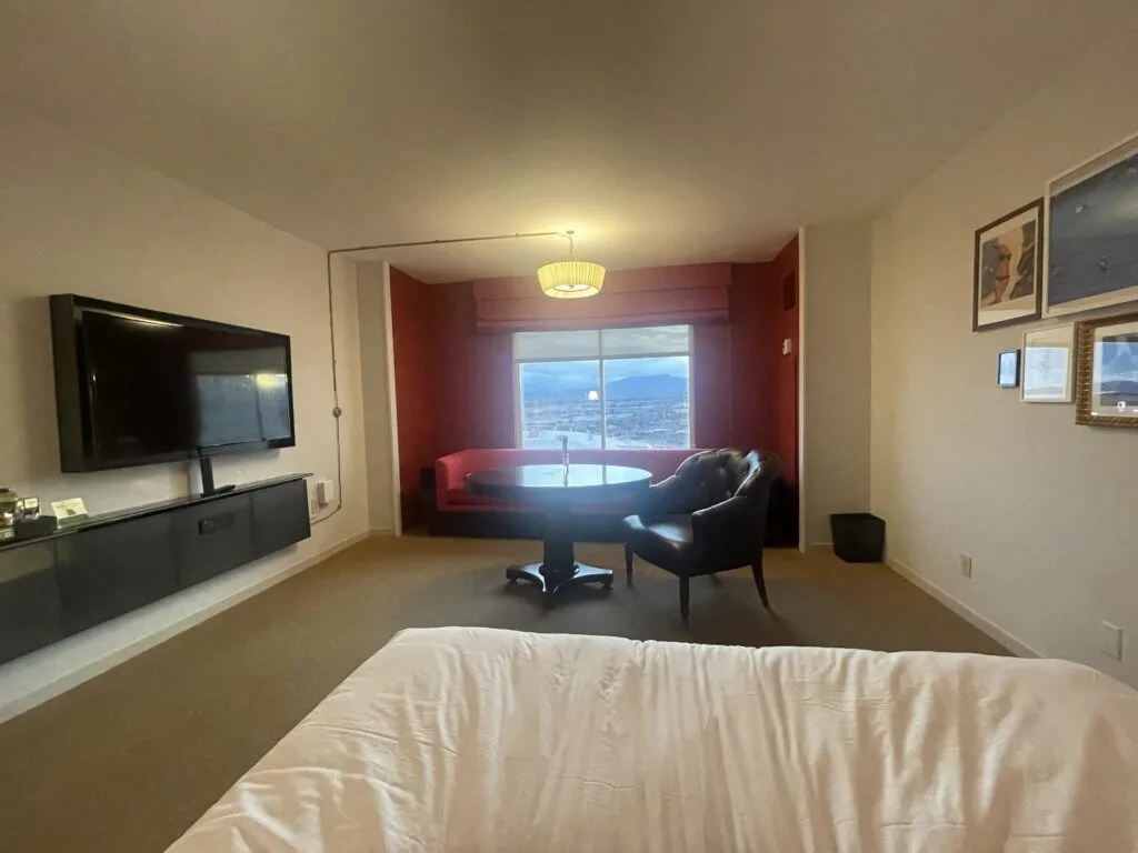 View of the room from the bed, with a TV mounted to the left and a window to the outdoors in the background.