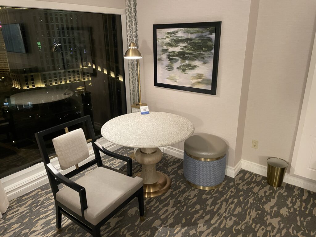 A small round table with a chair and a small stool type seat next to it. 
