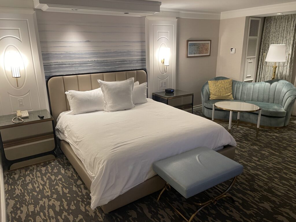 A king bed with a tuquise bench at the end. Flanking the bed are two end tables and lamps, which are turned on.